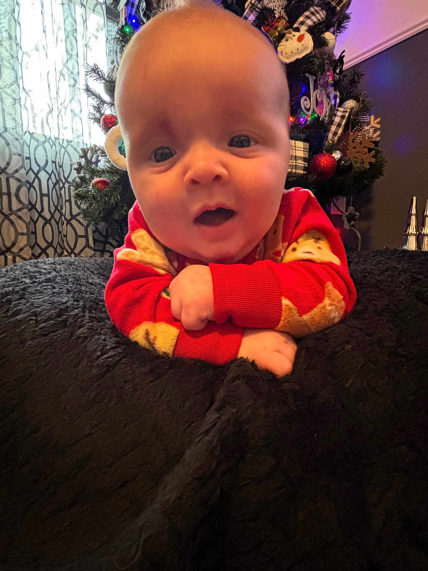 Adeline is registered to the contest to win money with this photo: baby, infant, christmas_tree, holiday, pajamas, red_clothing, blanket, face, smile, cute, indoors, ornament, decoration, curtain, living_room, person, close_up, soft_texture, hands, eyes