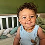 Sacha participe au concours pour gagner de l'argent avec cette photo : toddler, child, smile, curly_hair, blue_tank_top, necklace, crib, pillow, braided_cushion, bedroom, green_wall, indoor, soft_lighting, happy, person, infant, cute, portrait, baby, furniture