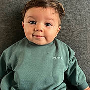 Sacha participe au concours pour gagner de l'argent avec cette photo : baby, child, face, smile, couch, green_sweatshirt, sitting, indoors, portrait, toddler, cute, clothing, hair, eyes, cozy, expression, furniture, sleeves, casual_wear, young