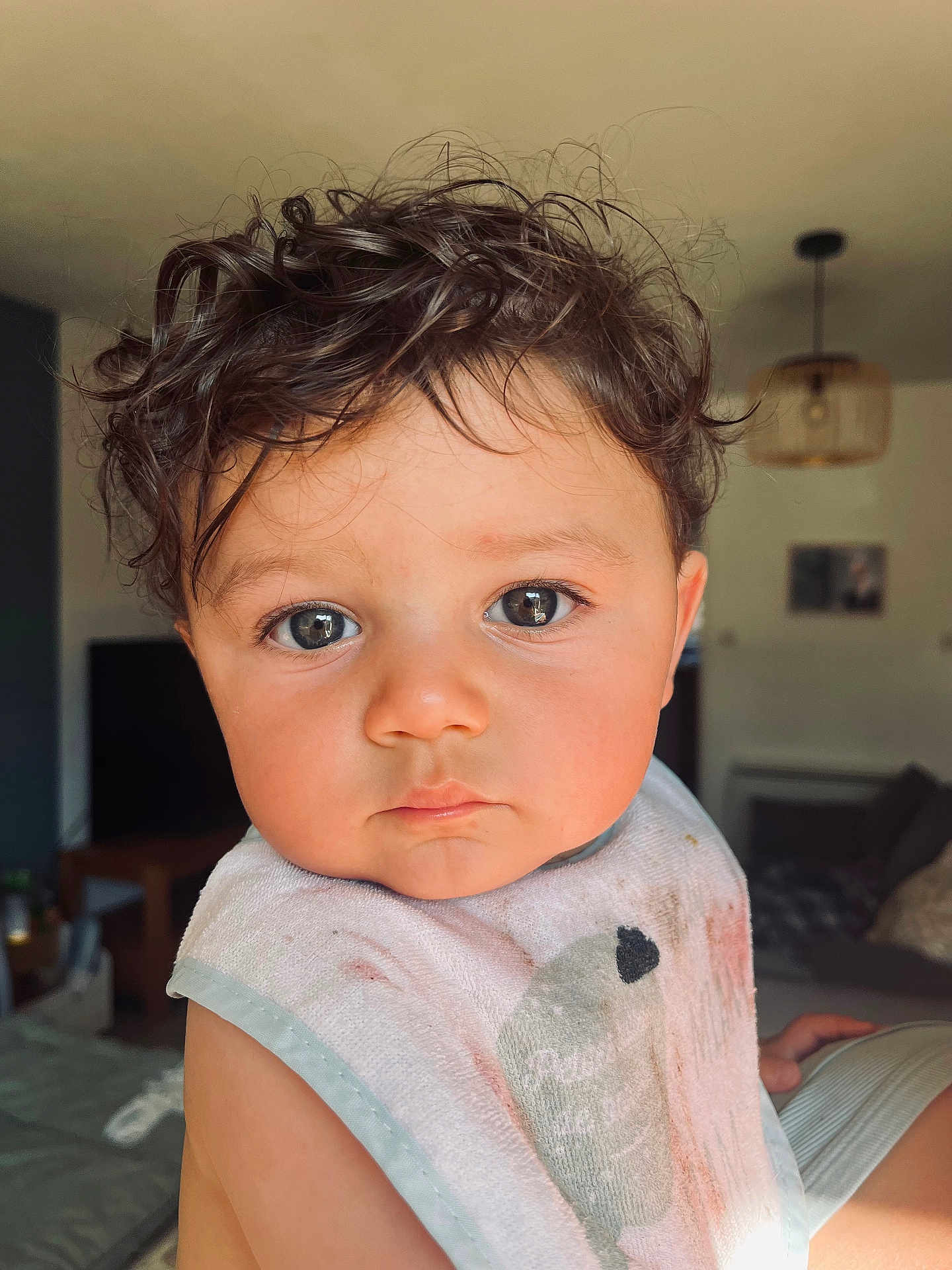 Sacha participe au concours pour gagner de l'argent avec cette photo : toddler, child, curly_hair, face, eyes, bib, indoor, portrait, expression, person, baby, skin, cute, living_room, furniture, soft_lighting, young_child, clothing, closeup, home