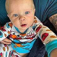 Bodie is registered to the contest to win money with this photo: baby, child, blue_eyes, pajamas, cookie_monster, elmo, drool, tattoo, person, arm, clothing, hand, face, indoor, closeup, cute, infant, looking_at_camera, sitting, holding