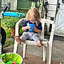 Raiden is registered to the contest to win money with this photo: child, toddler, blue_cup, plastic_chair, curly_hair, barefoot, backyard, green_shed, potted_plants, inflatable_pool, concrete, outdoor, summer, casual, drinking, grass, door, toy, bucket, play