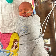 Lyla is registered to the contest to win money with this photo: newborn, baby, swaddled, hospital, feeding_tube, blanket, nursery, sleeping, tongue_out, medical_equipment, sheet, disney_princess, cartoon, girl_character, pacifier, bed, infant, cute, wrapped, clothing