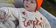 Charlie is registered to the contest to win money with this photo: toddler, child, orange_hat, pumpkin_sweater, knitwear, blanket, blue_jeans, metal_seat, yellow_background, cozy, casual, outdoor, cute, portrait, warm_colors, soft_texture, relaxed, young_child, fall_theme, fashion
