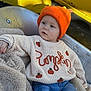 toddler, child, orange_hat, pumpkin_sweater, knitwear, blanket, blue_jeans, metal_seat, yellow_background, cozy, casual, outdoor, cute, portrait, warm_colors, soft_texture, relaxed, young_child, fall_theme, fashion