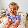 baby, blue_eyes, child, clean_background, cushion, cute, daisy_pattern, face, feet, hands, happy, indoor, infant, natural_light, person, purple_clothing, sitting, smiling, toddler, wooden_floor