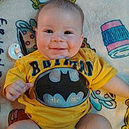 Riott is registered to the contest to win money with this photo: baby, child, smile, batman, yellow_shirt, diaper, blanket, pacifier, cute, infant, sitting, happy, chubby_cheeks, indoor, person, clothing, face, head, young, playful