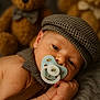 baby, pacifier, hat, teddy_bear, blurred_background, suspenders, infant, cute, sleepy, closeup, soft_texture, child, face, hand, bedroom, plush, resting, portrait, newborn, warm_lighting
