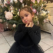 Leana a rejoint le concours — aidez-le/la à gagner de superbes lots ! child, girl, black_dress, christmas_tree, holiday_decorations, pink_bows, ornaments, twinkling_lights, indoor, floor_tiles, pose, cute, festive, holiday, smile, person, celebration, home, winter, festivity