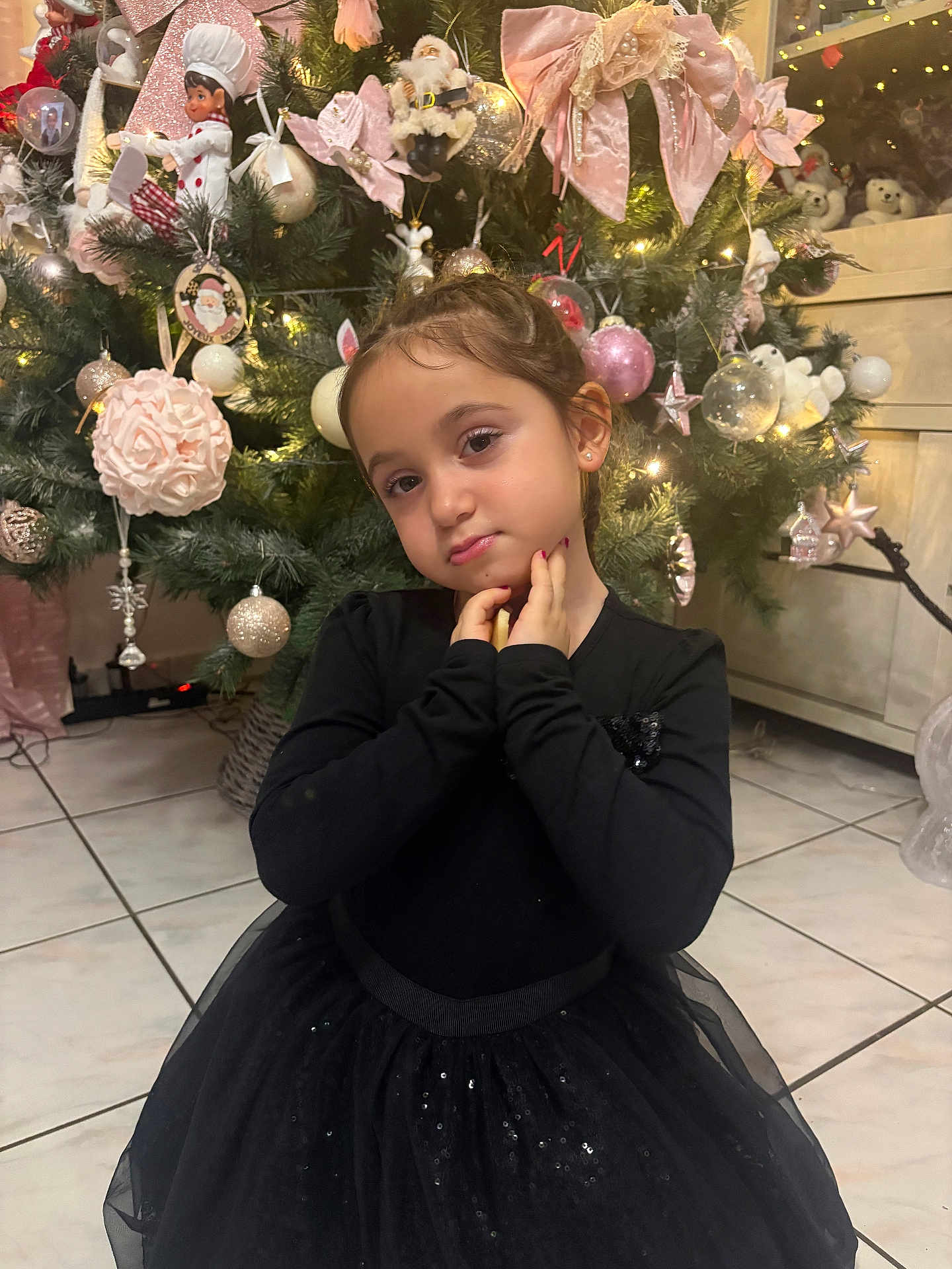 Leana a rejoint le concours — aidez-le/la à gagner de superbes lots ! child, girl, black_dress, christmas_tree, holiday_decorations, pink_bows, ornaments, twinkling_lights, indoor, floor_tiles, pose, cute, festive, holiday, smile, person, celebration, home, winter, festivity