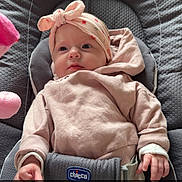 Lya participe au concours pour gagner de l'argent avec cette photo : baby, infant, child, car_seat, chicco, headband, bow, pink_clothing, hoodie, harness, seat_belt, plush_toy, padded_seat, portrait, face, eyes, hands, cozy, indoor, heart_emoji