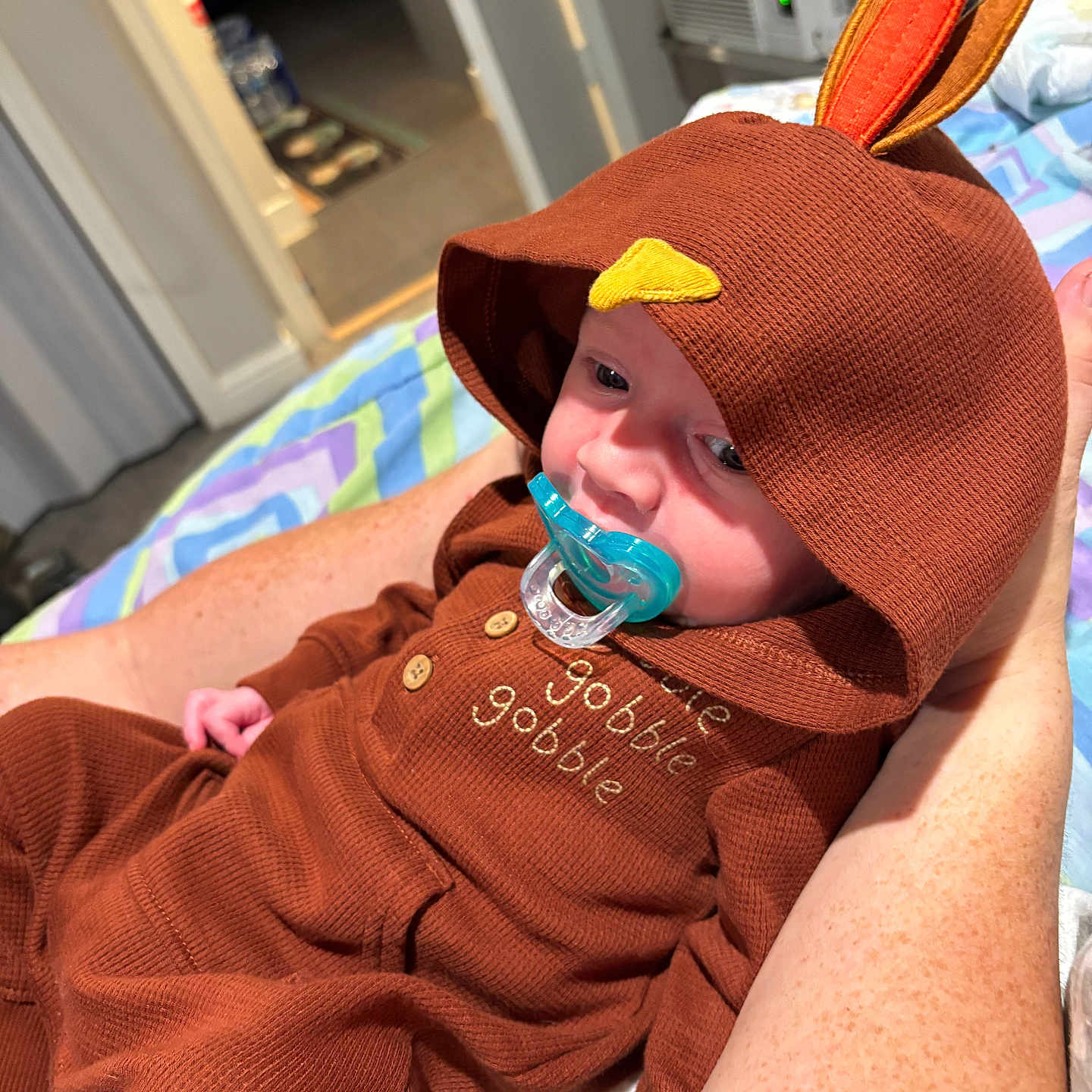 Noah joined the competition — help win amazing prizes! arm, baby, bedroom, blanket, brown_clothing, button, child, comfort, cute, fabric, hand, hood, indoor, infant, pacifier, patterned_blanket, person, resting, sleepy, turkey_costume