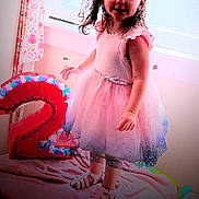 Khloe is registered to the contest to win money with this photo: child, birthday, dress, crown, number_two, pink, curtains, bed, toy, unicorn, indoor, happy, celebration, footwear, person, smiling, decorations, party, girl, window