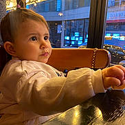 Alaïa-Victoria a rejoint le concours — aidez-le/la à gagner de superbes lots ! toddler, child, pony_tail, indoor, table, wooden_table, window, city_lights, reflection, warm_lighting, clothing, long_sleeves, face, expression, curious, seated, restaurant, evening, urban, chair