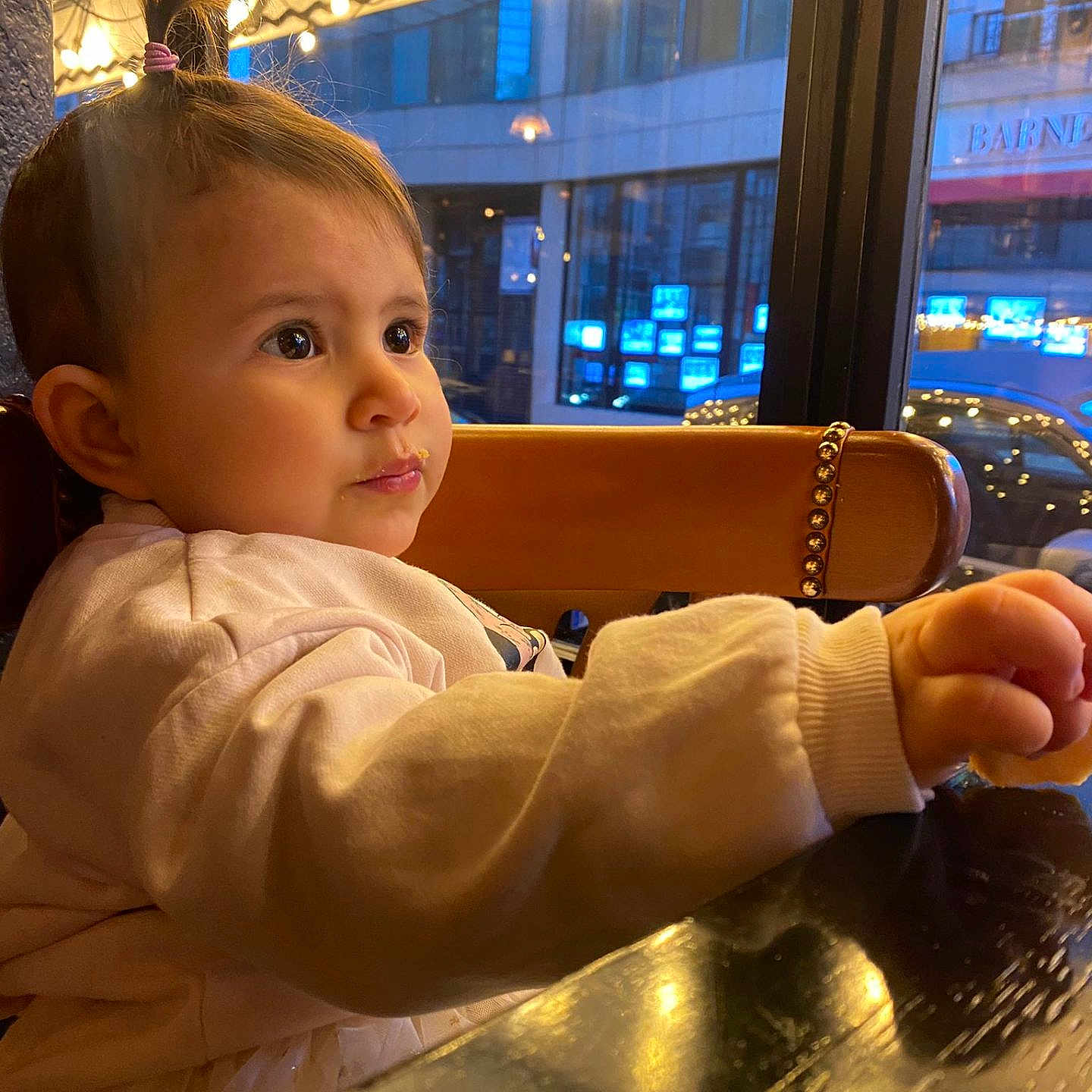 Alaïa-Victoria a rejoint le concours — aidez-le/la à gagner de superbes lots ! chair, child, city_lights, clothing, curious, evening, expression, face, indoor, long_sleeves, pony_tail, reflection, restaurant, seated, table, toddler, urban, warm_lighting, window, wooden_table