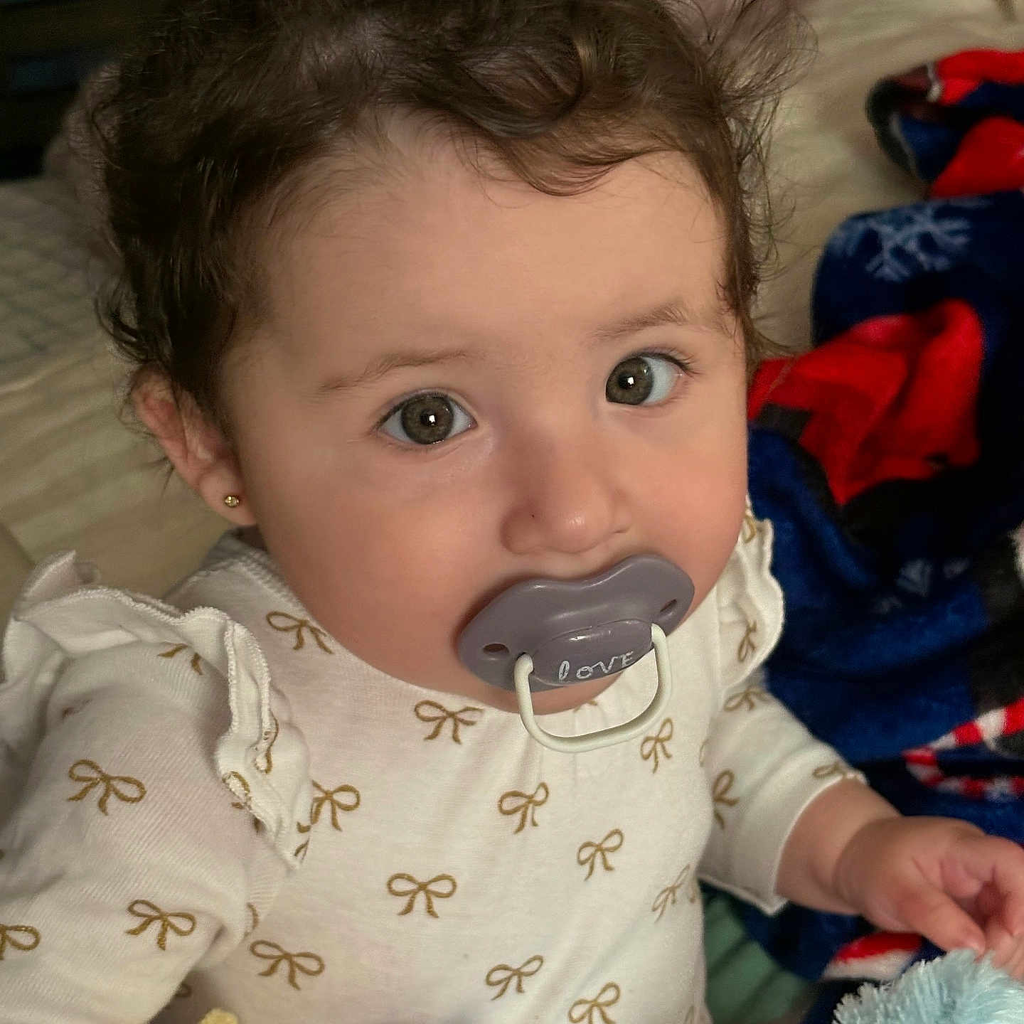 Maialen is registered to the contest to win money with this photo: baby, blanket, bow, child, clothing, cozy, curly_hair, cute, earrings, face, hands, indoors, infant, long_sleeve, looking_at_camera, pacifier, plush_toy, portrait, sitting, soft_toys