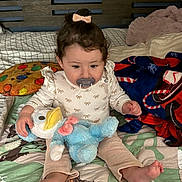 Maialen is registered to the contest to win money with this photo: toddler, pacifier, plush_toy, bed, blanket, pillow, bow, child, indoor, cute, clothing, sitting, person, foot, hand, face, hair, soft_toy, comfort, cozy
