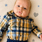 Maveryck is registered to the contest to win money with this photo: baby, infant, plaid_shirt, navy_pants, lying_down, face, eyes, hand, patterned_blanket, stars, hearts, cute, child, portrait, indoors, soft_light, clothing, young, person, baby_boy