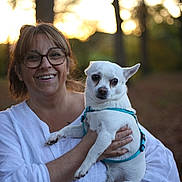 Shelby participe au concours pour gagner de l'argent avec cette photo : animal, casual, daylight, dog, forest, glasses, happy, holding, leash, nature, outdoor, person, pet, portrait, small_dog, smile, sunset, trees, white_clothing, woman