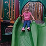 Gracielynn is registered to the contest to win money with this photo: child, girl, slide, playground, green_slide, pink_shirt, blue_pants, outdoor, trees, play_equipment, smiling, casual_clothing, fun, recreation, daytime, nature, leisure, cute, active, young