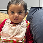 Ojasvita joined the competition — help win amazing prizes! baby, infant, child, face, eyes, clothing, bib, sitting, couch, cushion, indoor, skin, expression, person, cute, young, head, hair, portrait, comfort