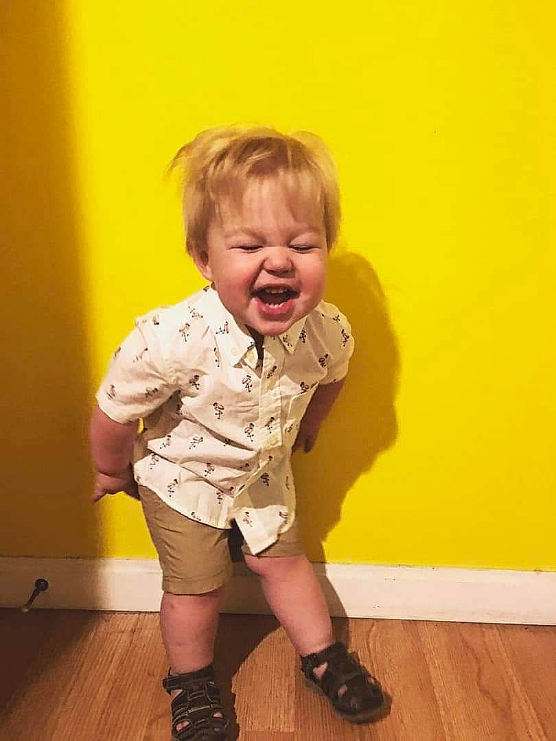 Adam is registered to the contest to win money with this photo: blond, cheek, child, facial_expression, knee, laugh, leg, person, play, shoe, sitting, skin, sleeve, smile, standing, t_shirt, toddler, yellow