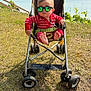 baby, stroller, sunglasses, red_clothing, grass, outdoor, sea, sky, greenery, child, footwear, barefoot, reflection, sunny, summer, nature, casual, cute, portrait, person