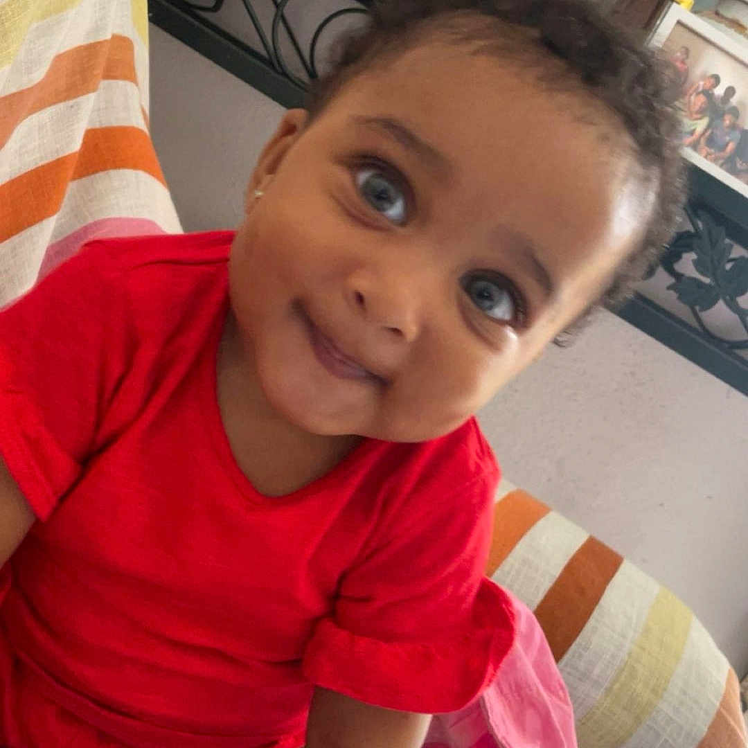 Eva Maria participe au concours pour gagner de l'argent avec cette photo : candid, casual, cheeky, child, close_up, cross_legged, curly_hair, cute, family_photos, happy, home_decor, indoor, person, portrait, red_clothing, sitting, smiling, striped_couch, toddler, young_child