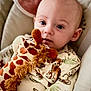 baby, child, plush_toy, giraffe, onesie, animal_print, cushion, seat, indoor, portrait, cute, infant, soft_toy, cozy, young_child, looking_at_camera, closeup, head, face, expression
