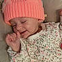 baby, infant, pink_hat, knit_hat, bow, heart, floral_onesie, cushion, smiling, happy, sleepy, cute, child, portrait, cozy, indoor, soft_lighting, relaxed, small_hand, lying_down