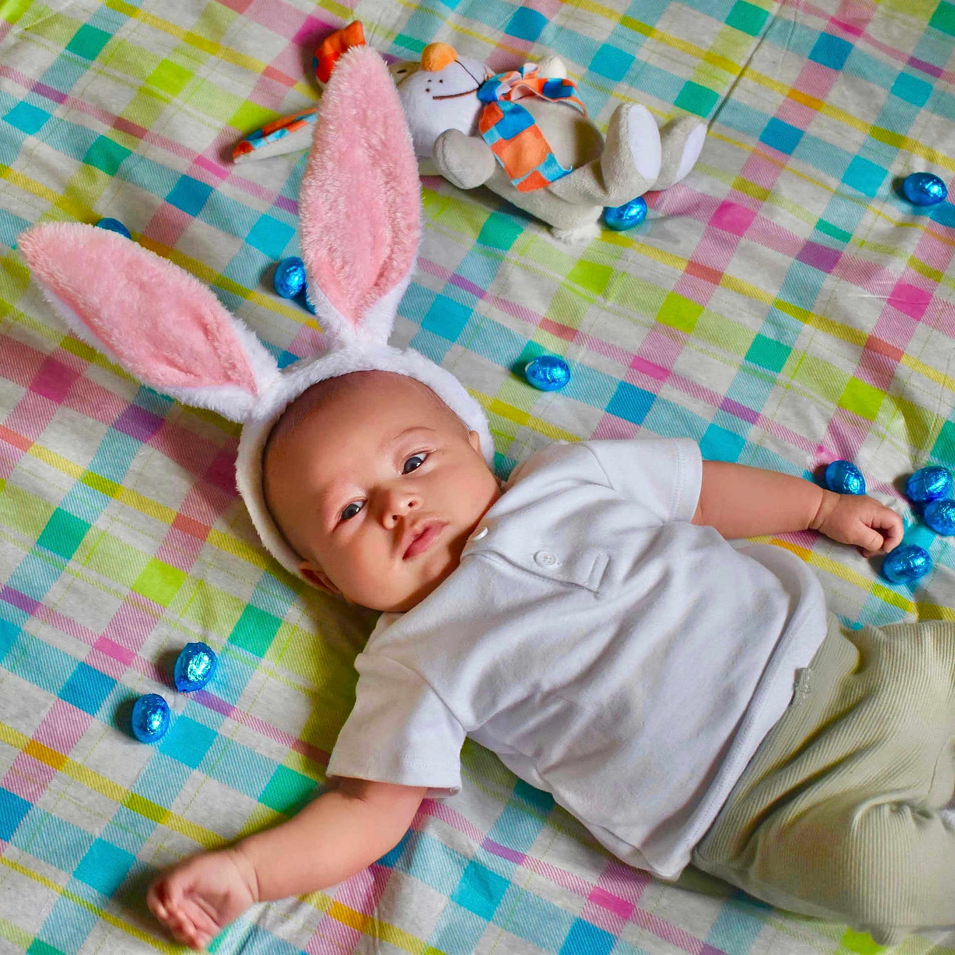 Gabriel participe au concours pour gagner de l'argent avec cette photo : baby, blanket, bunny_ears, child, colorful, cute, easter_eggs, green_pants, headwear, holiday_theme, indoors, infant, lying_down, plaid_pattern, playful, relaxed, soft_toy, stuffed_animal, toy, white_shirt