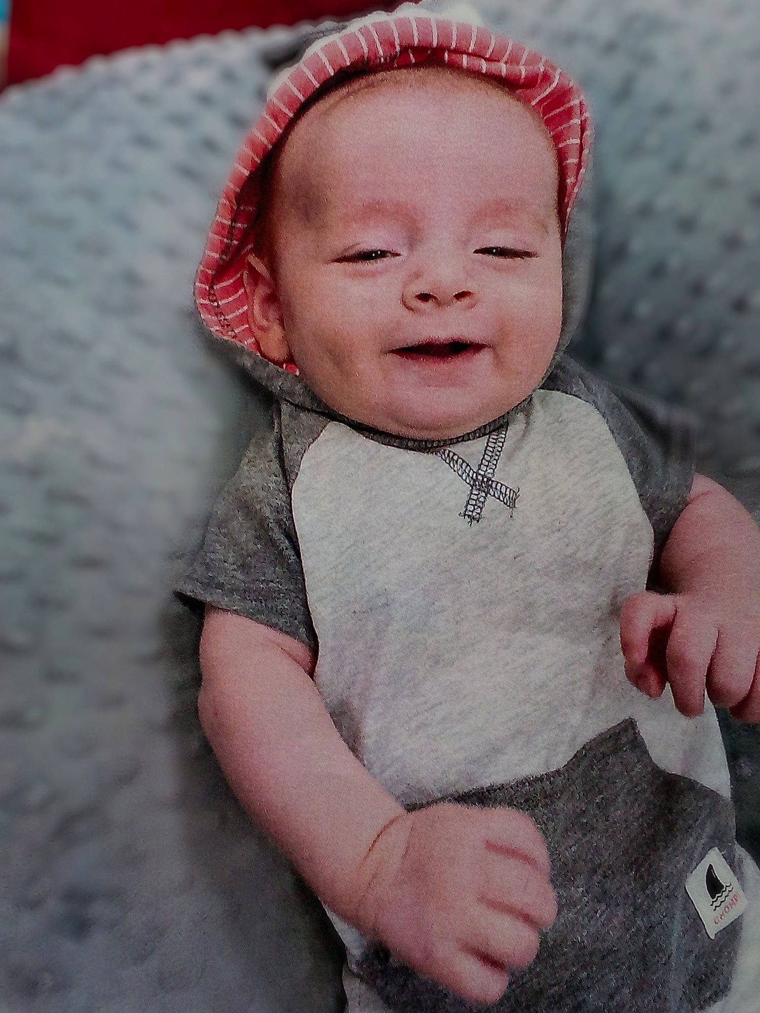 King is registered to the contest to win money with this photo: baby, baby_toddler_clothing, cap, cheek, chin, eye, face, gesture, grey, happy, head, human_body, iris, lip, nose, person, pink, skin, sleeve, smile
