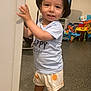 toddler, child, hat, bucket_hat, shirt, shorts, sandals, indoor, toys, playroom, smile, standing, door_frame, happy, person, footwear, colorful, floor, expression, casual
