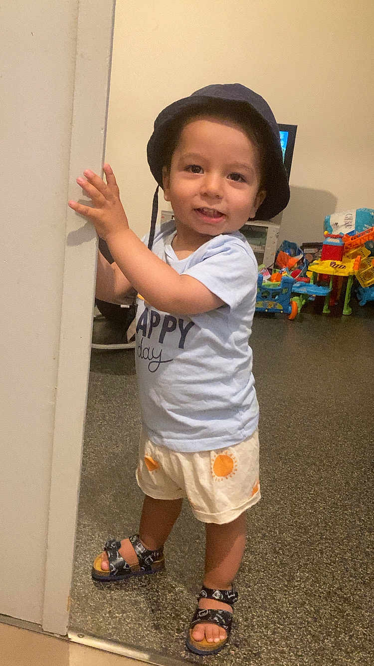 Kelio Leonard a rejoint le concours — aidez-le/la à gagner de superbes lots ! toddler, child, hat, bucket_hat, shirt, shorts, sandals, indoor, toys, playroom, smile, standing, door_frame, happy, person, footwear, colorful, floor, expression, casual