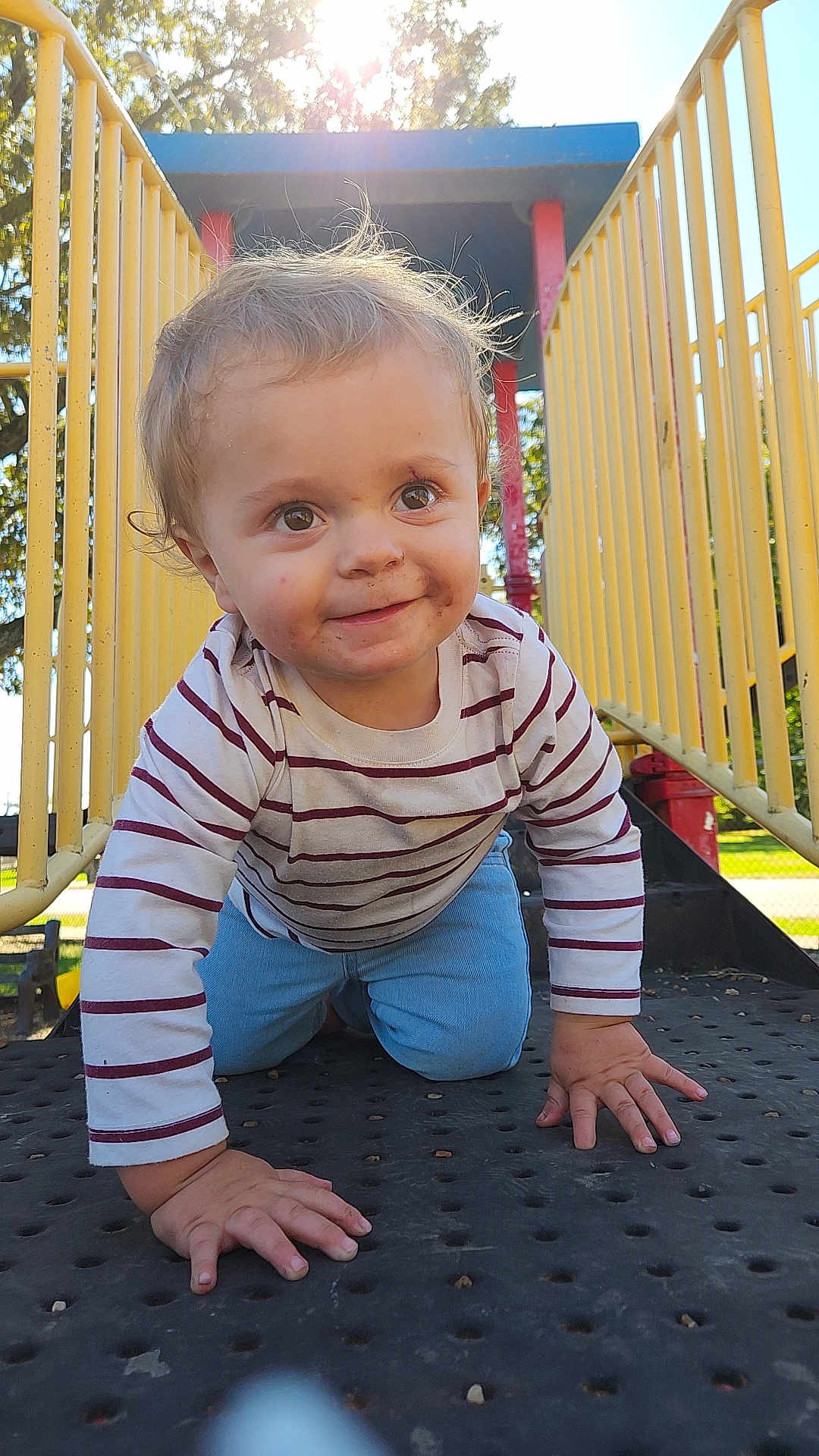 Abaddon joined the competition — help win amazing prizes! toddler, child, playground, yellow_railings, striped_shirt, blue_pants, outdoor, sunlight, smiling, crawling, metal_platform, daylight, trees, face, hands, curly_hair, play_structure, happy, nature, park