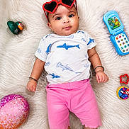 Sukhmn joined the competition — help win amazing prizes! baby, child, heart_shaped_sunglasses, pink_shorts, white_shirt, shark_print, toy_phone, green_duck_toy, pink_ball, fluffy_rug, lying_down, cute, infant, bracelet, colorful_toys, playtime, indoor, portrait, happy, curious