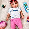 baby, child, heart_shaped_sunglasses, pink_shorts, white_shirt, shark_print, toy_phone, green_duck_toy, pink_ball, fluffy_rug, lying_down, cute, infant, bracelet, colorful_toys, playtime, indoor, portrait, happy, curious