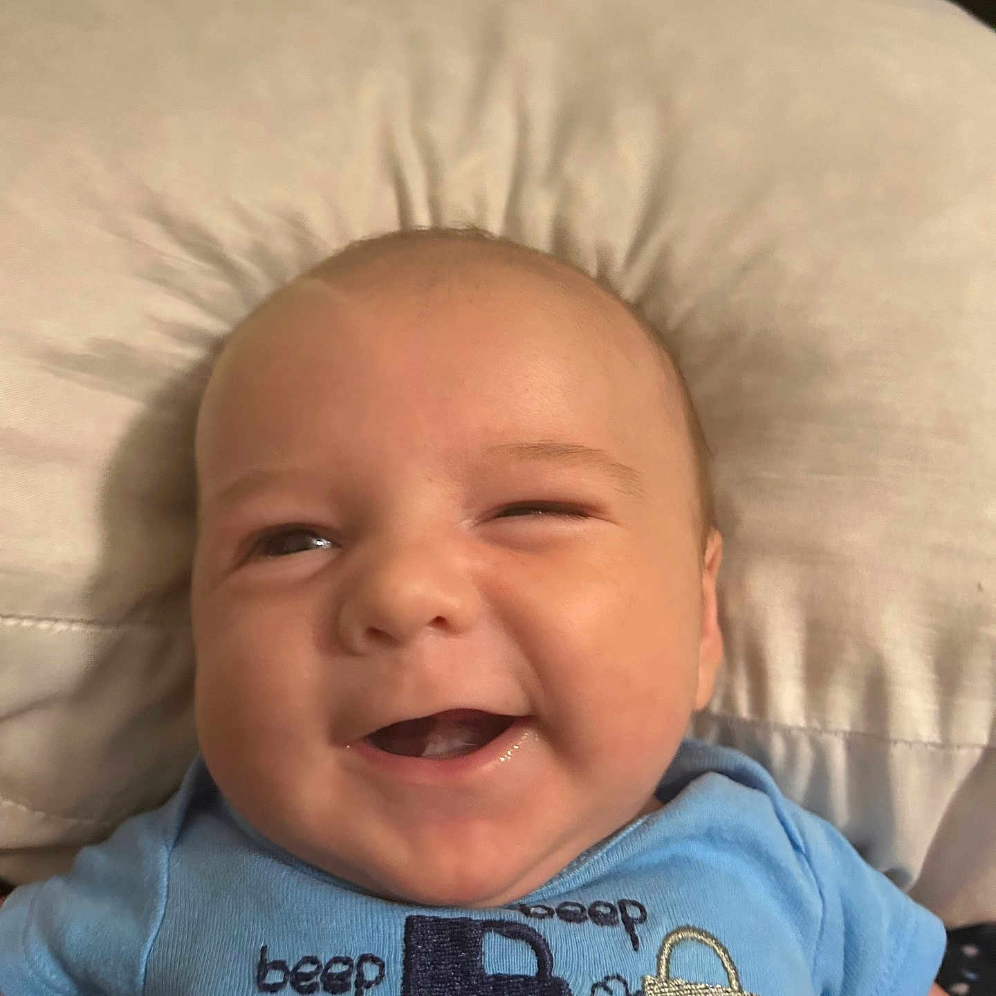 Woodrow is registered to the contest to win money with this photo: baby, smiling, blue_onesie, car_embroidery, pillow, face, happy, infant, child, cute, portrait, closeup, expression, skin, head, clothing, indoors, person, baby_garment, newborn