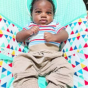Kaden is registered to the contest to win money with this photo: baby, child, infant, striped_shirt, beige_pants, mouse_ears, baby_chair, colorful_pattern, triangles, white_socks, cute, portrait, indoors, seated, young_child, curious, hands_clenched, comfort, soft_lighting, closeup