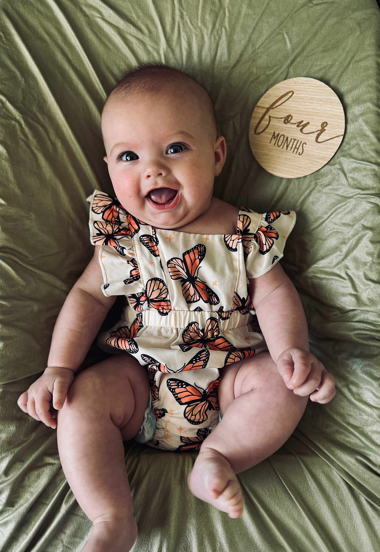 Noelle is registered to the contest to win money with this photo: baby, butterfly_pattern, child, chubby_legs, clothing, cute, face, four_months, green_blanket, happy, head, indoor, infant, milestone, portrait, sitting, skin, smiling, wooden_plaque, young_baby