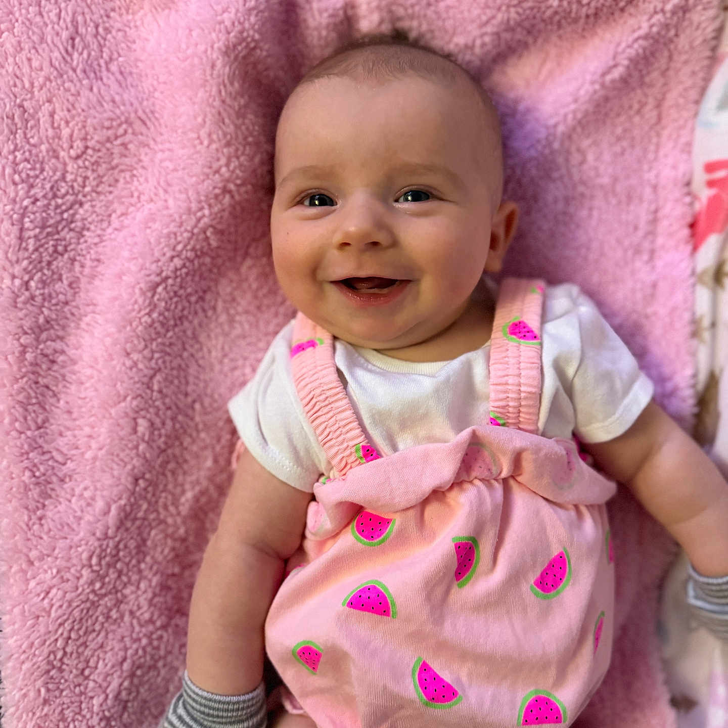 Oakley is registered to the contest to win money with this photo: baby, infant, smile, pink_blanket, pink_outfit, watermelon_pattern, mittens, happy, cute, lying_down, child, face, portrait, soft_texture, apparel, cheerful, young_child, skin, head, expression