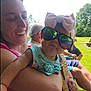 Loretta is registered to the contest to win money with this photo: baby, woman, outdoor, sunglasses, bow, headband, greenery, grass, trees, smile, happy, child, person, sunlight, summer, casual_clothing, family, nature, relaxation, fun