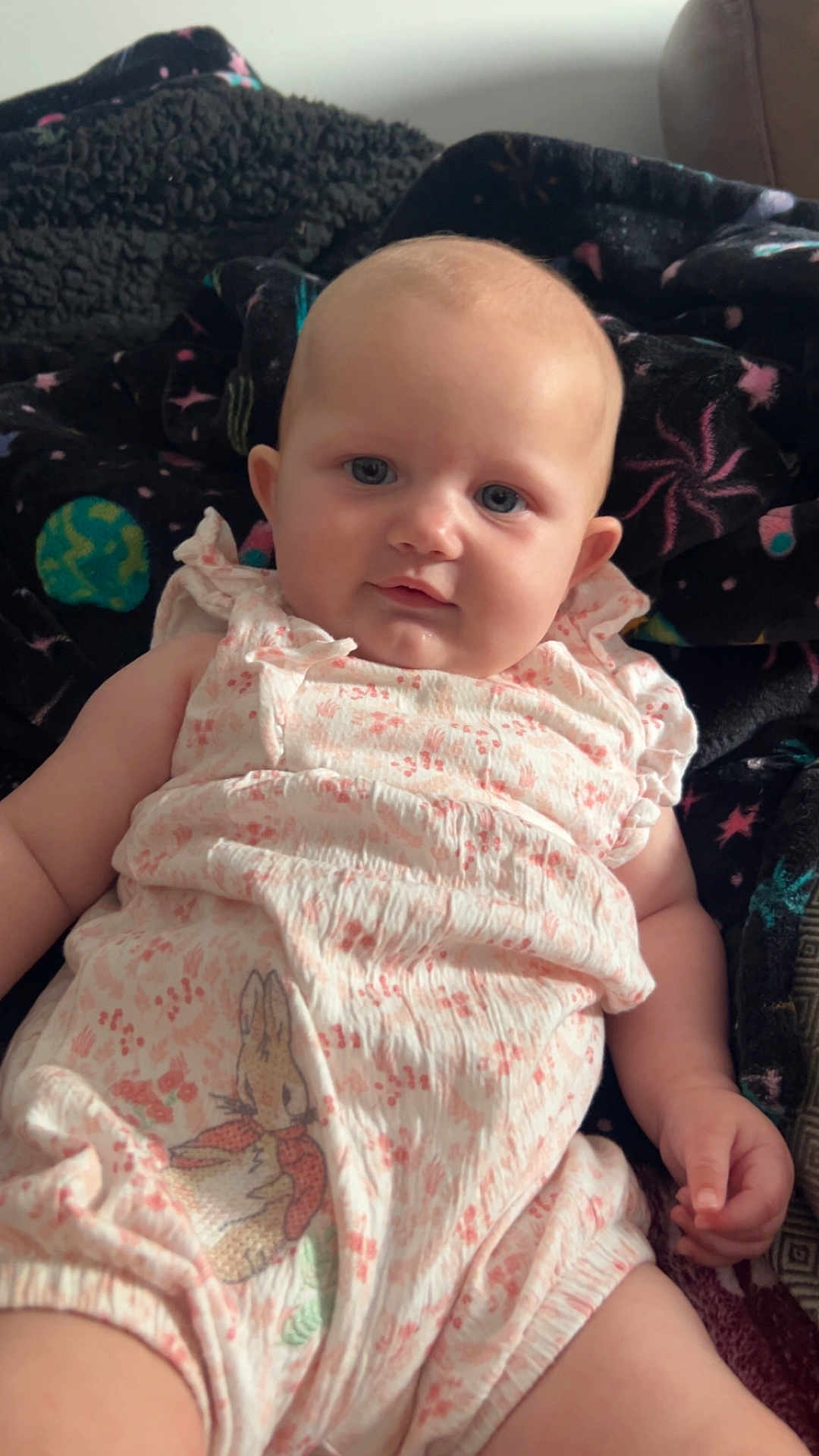 Lyla joined the competition — help win amazing prizes! baby, infant, romper, floral_pattern, bunny_print, blanket, galaxy_pattern, blue_eyes, skin, face, chubby_cheeks, arm, hand, soft_light, indoor, portrait, clothing, comfort, lying_down, cute