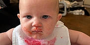 Lyla joined the competition — help win amazing prizes! baby, bib, high_chair, food_stains, messy, indoor, face, expression, child, person, blue_eyes, clothing, skin, head, hairless, mouth, nose, furniture, room, floor