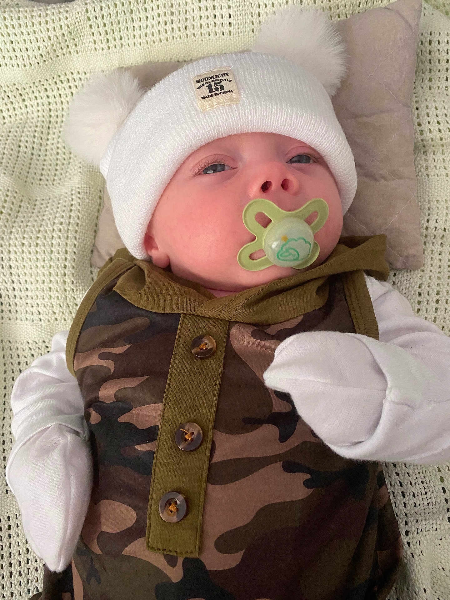 Alexander joined the competition — help win amazing prizes! baby, pacifier, hat, mittens, camo_clothing, blanket, pillow, infant, face, person, newborn, cute, sleepy, comfort, soft, resting, indoor, portrait, headwear, child