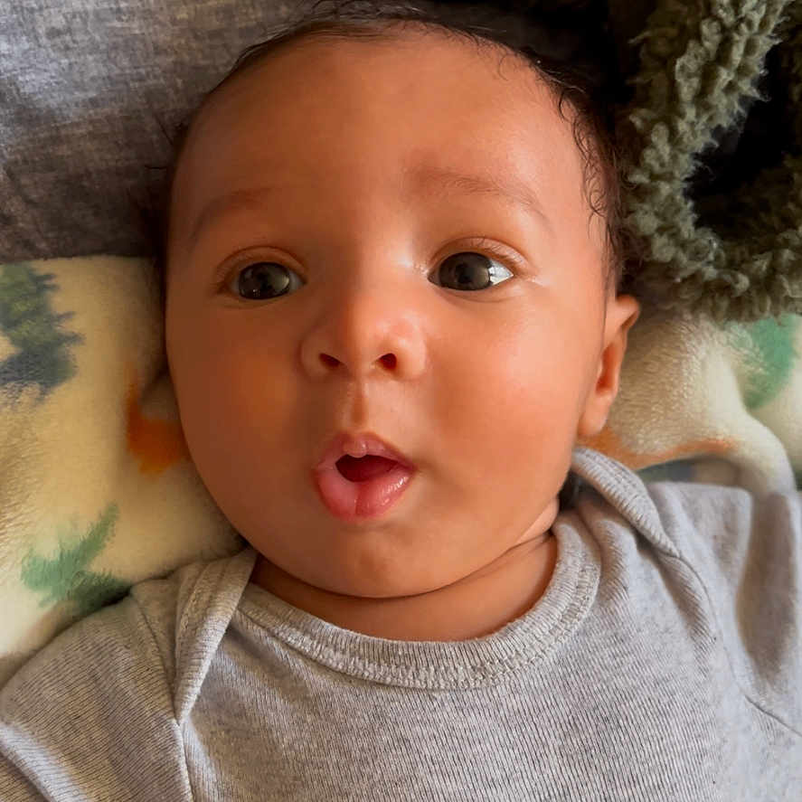 Dashaun joined the competition — help win amazing prizes! baby, blanket, child, clothing, cozy, curious, cute, expression, eyes, face, head, indoor, infant, lying_down, mouth, onesie, portrait, skin, soft_texture, young