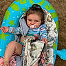 baby, infant, pacifier, blue_inflatable, pool_float, quilt, patchwork, deer_pattern, floral_pattern, sandy_background, child, smiling, playful_hairstyle, barefoot, outdoor, relaxed, colorful_clothing, blanket, cute, portrait