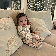 Louise participe au concours pour gagner de l'argent avec cette photo : toddler, child, pajamas, couch, pillows, indoor, home, cozy, soft_lighting, curly_hair, patterned_clothing, neutral_colors, infant, seated, plush, relaxed, portrait, baby, living_room, comfort