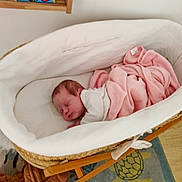 Isaé a rejoint le concours — aidez-le/la à gagner de superbes lots ! newborn, baby, sleeping, bassinet, blanket, pink, white, wooden, crib, child, indoor, cozy, soft, peaceful, home, floor_rug, turtle, book, furniture, resting