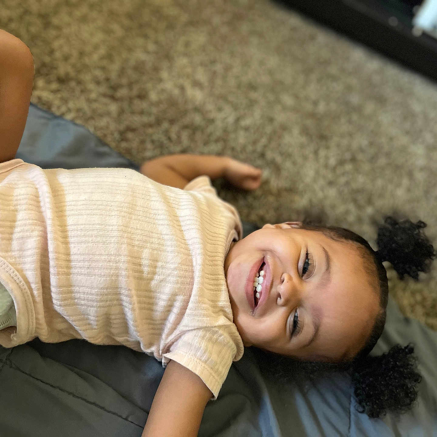Ryyah joined the competition — help win amazing prizes! child, toddler, girl, smiling, happy, portrait, curly_hair, teeth, lying_down, indoor, carpet, blanket, bed, clothing, shirt, diaper, arm, face, home, photography